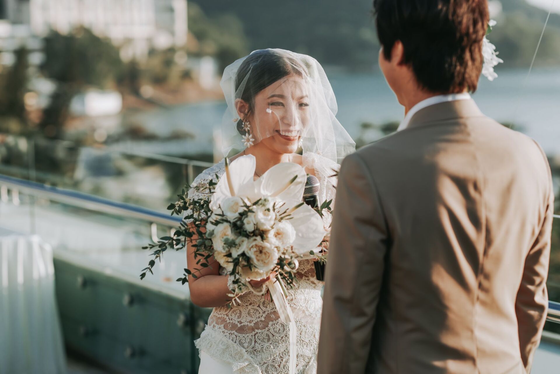 Bride and groom at outdoor wedding ceremony. Bride holds bouquet, looks at groom with emotional expression.