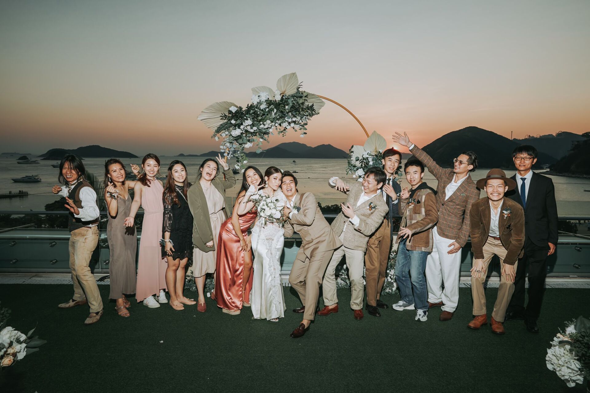 Wedding group photo on a rooftop at sunset, posing, with floral arch.