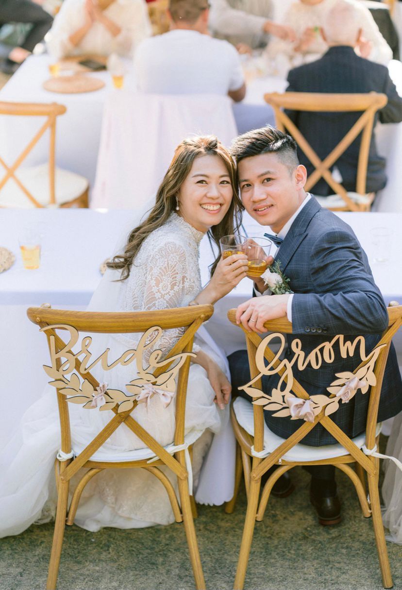 Bride and groom at a wedding reception, toasting. Bride in white lace dress, groom in blue suit. 