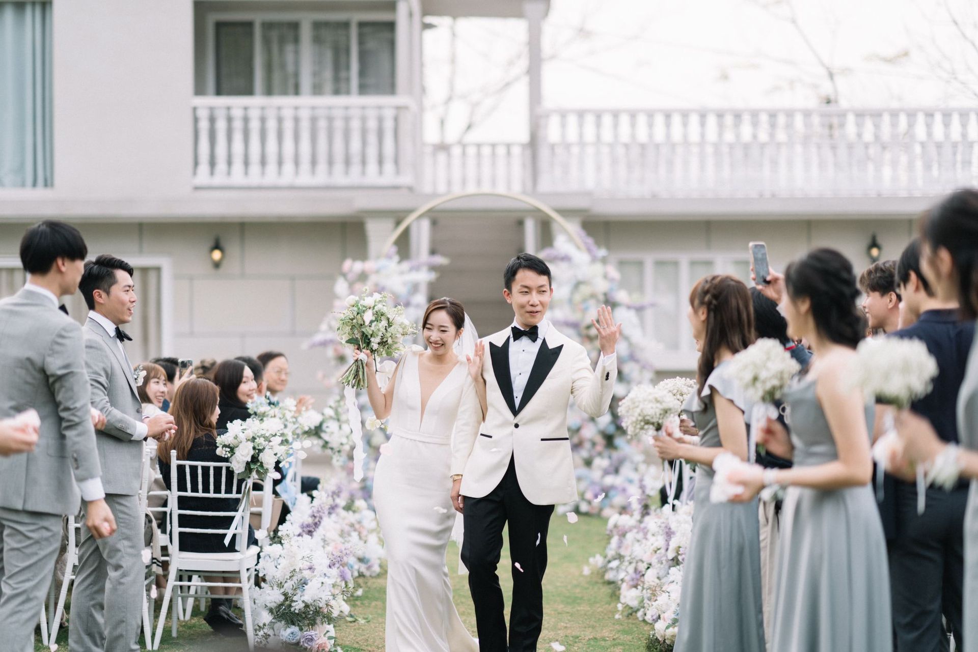 Newlyweds walk down aisle after ceremony, surrounded by wedding party and floral decorations.