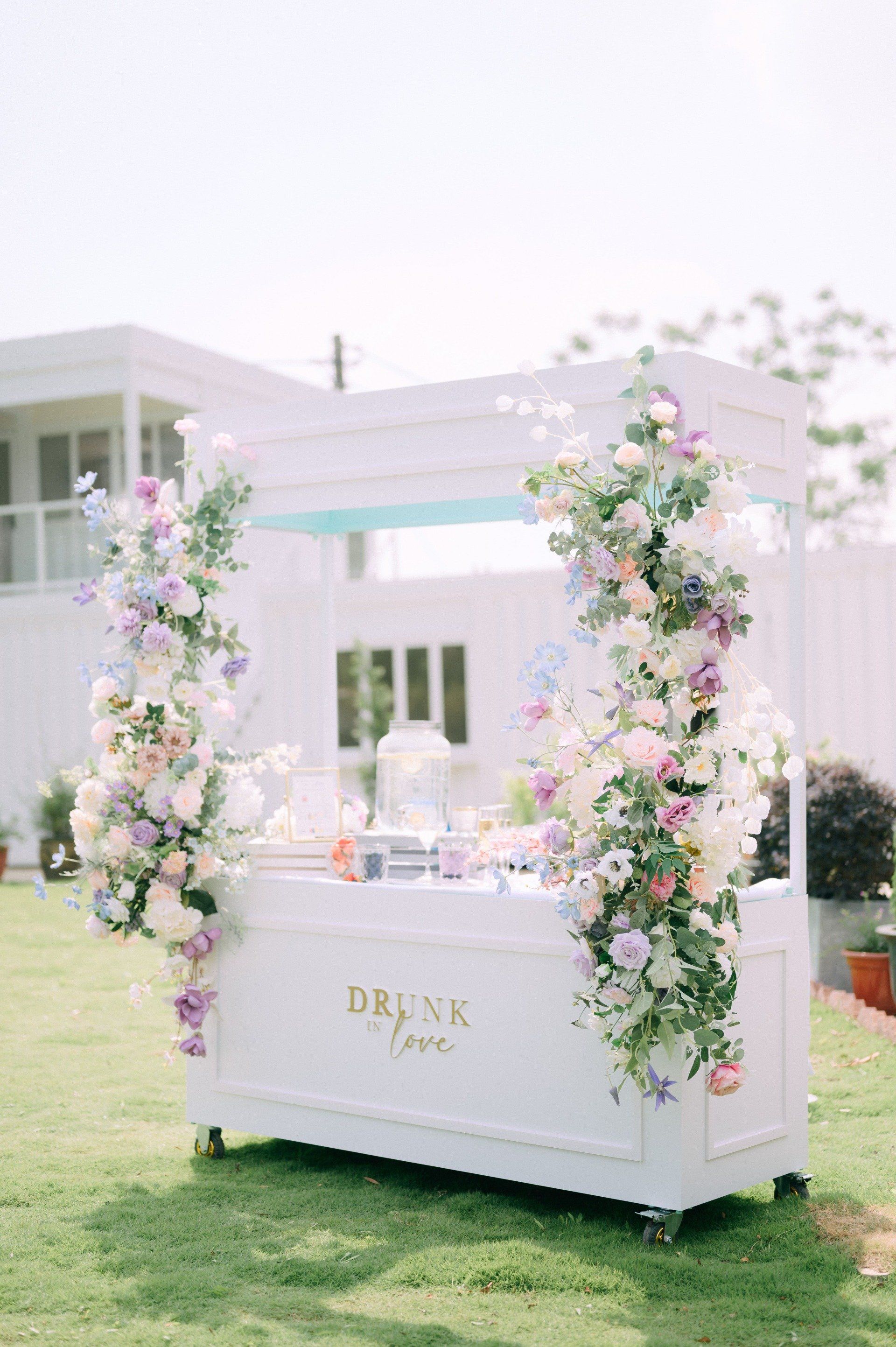 White drink cart decorated with pastel flowers on green grass. 
