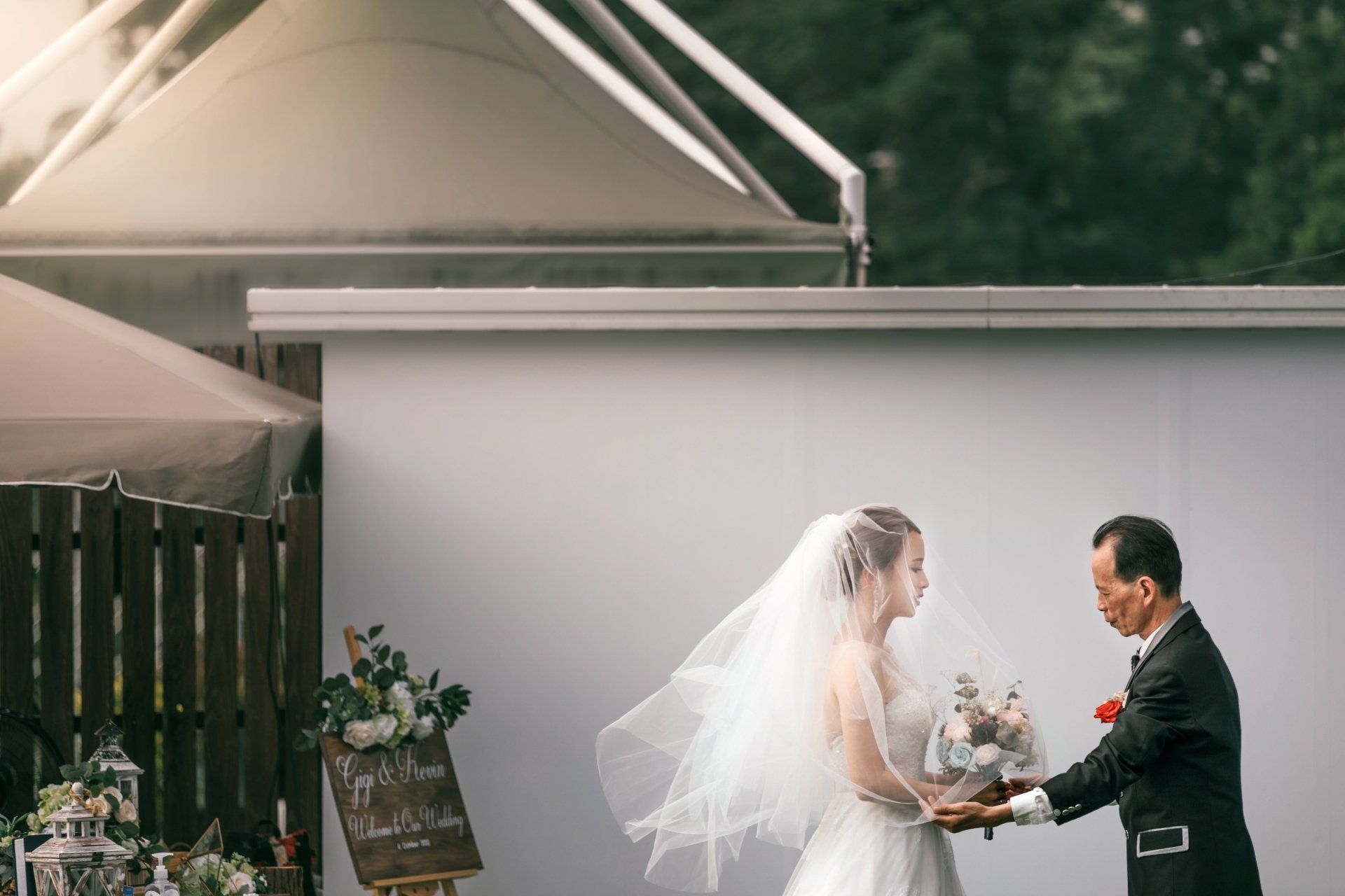 Bride and man hold hands during outdoor wedding ceremony. Bride in white dress and veil, man in suit.