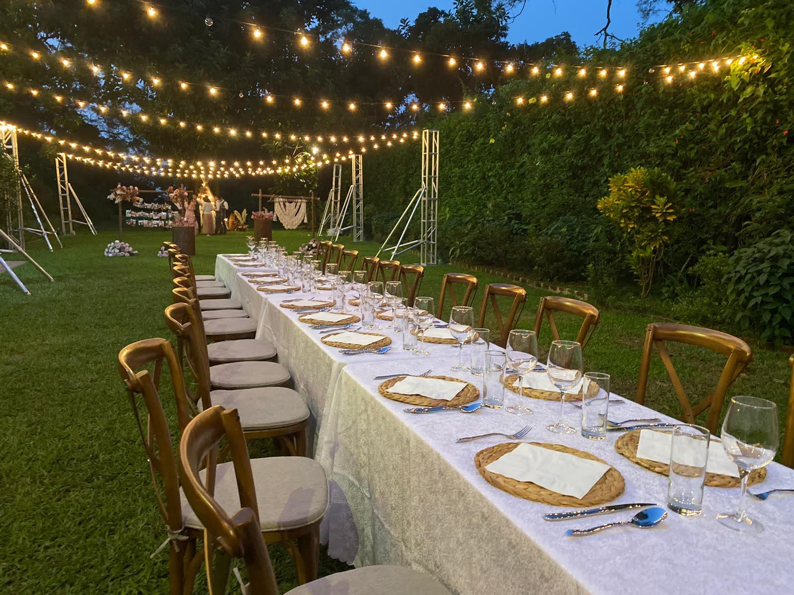 Long outdoor dinner table set for an event, with string lights overhead.