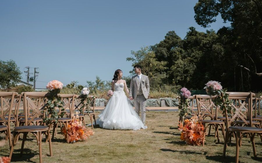 Couple at an outdoor wedding ceremony, walking towards each other, surrounded by chairs and floral arrangements.