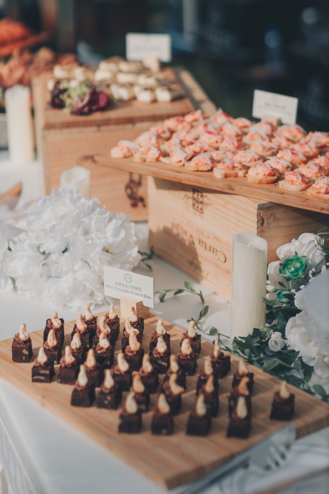 Buffet table with appetizers on wooden platters: salmon bites, cheese, and chocolate treats.