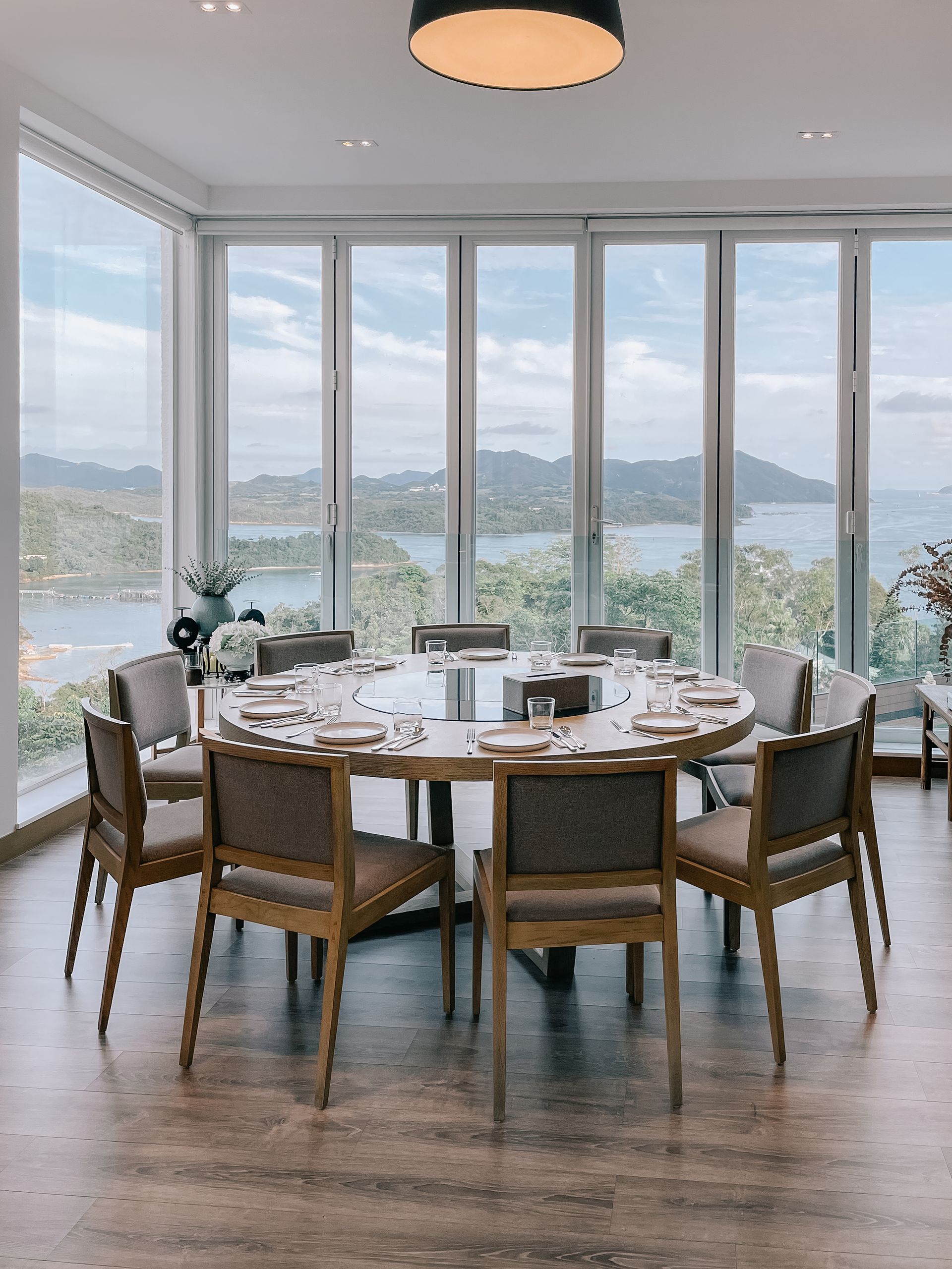 Round dining table with chairs, floor-to-ceiling windows overlooking a scenic waterfront view.