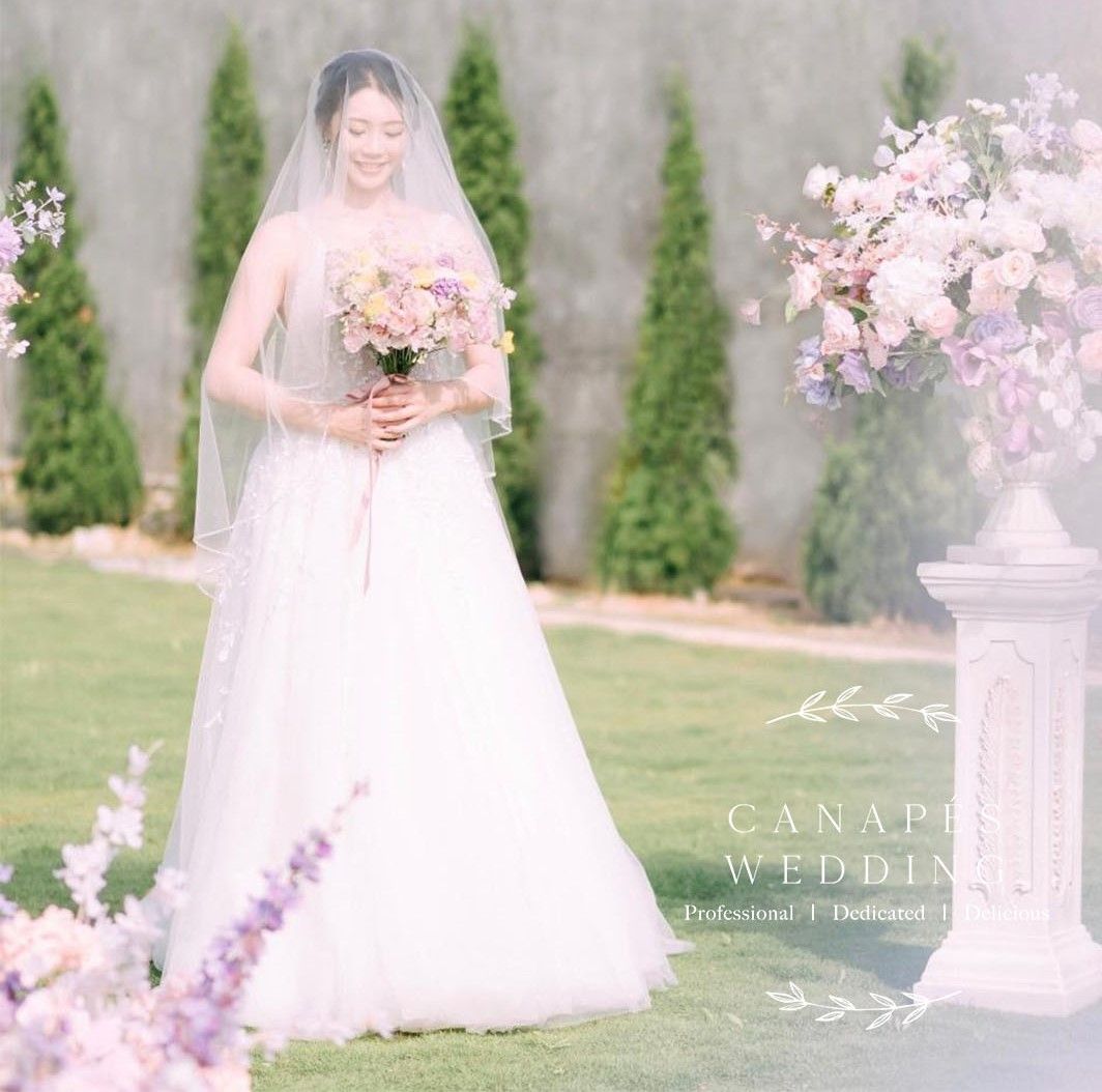 Bride in white wedding dress holding bouquet, standing outdoors.