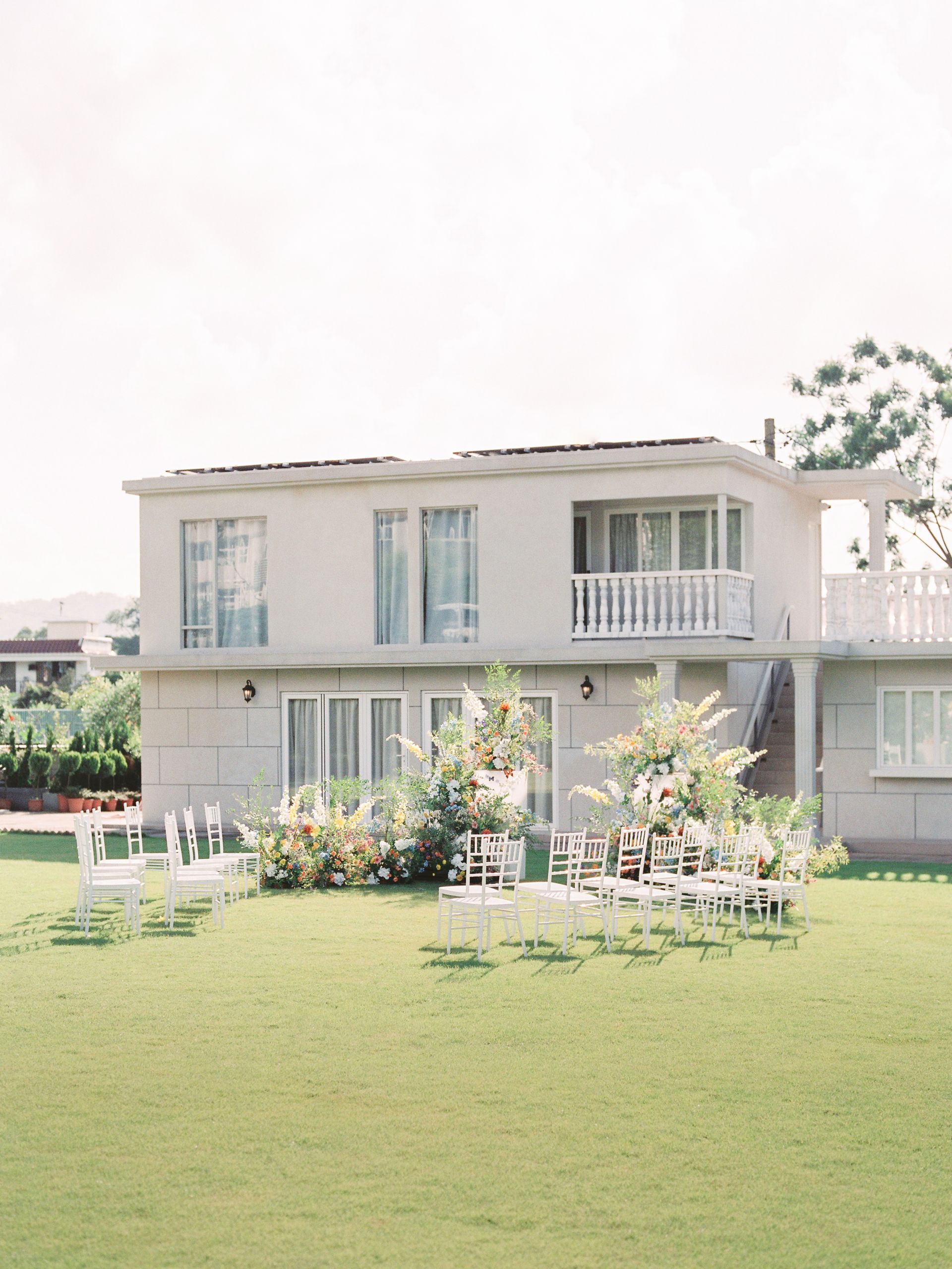 Two-story white building with a balcony overlooking a grassy lawn with white chairs.