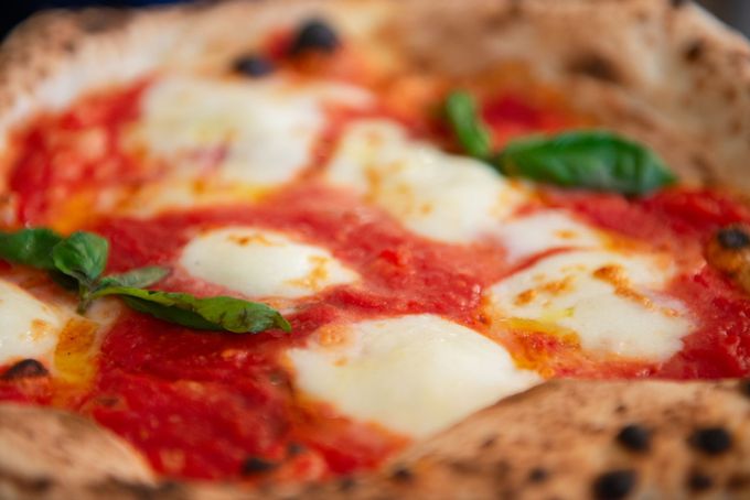 Primo piano di una pizza Margherita con salsa di pomodoro, mozzarella fusa e foglie di basilico su una crosta bruciacchiata.