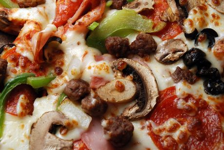 Primo piano di una pizza condita con funghi, peperoni, olive, salsiccia e formaggio fuso.