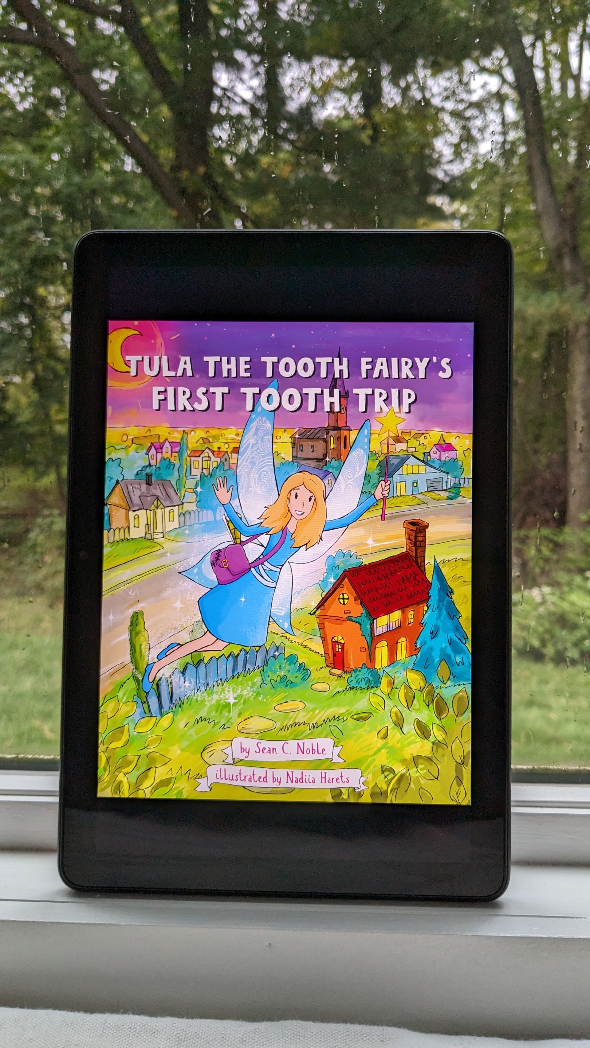 A tablet is sitting on a window sill with a book on it.