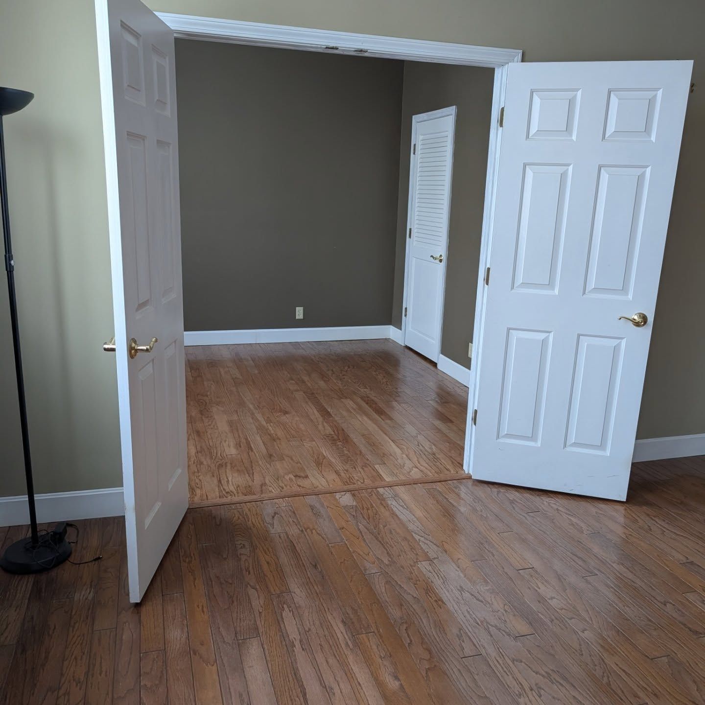 Open white double doors reveal an empty room with wood floors and tan walls
