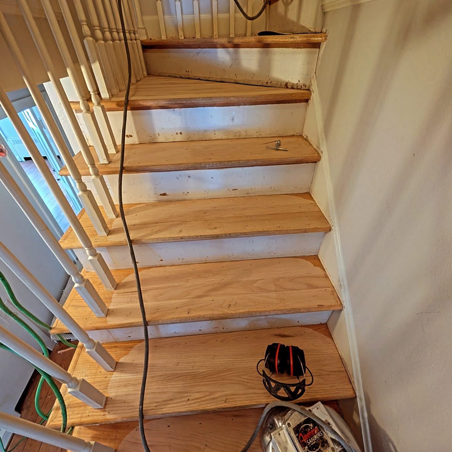 Wooden staircase under construction with unfinished steps, railing, and tools on the floor