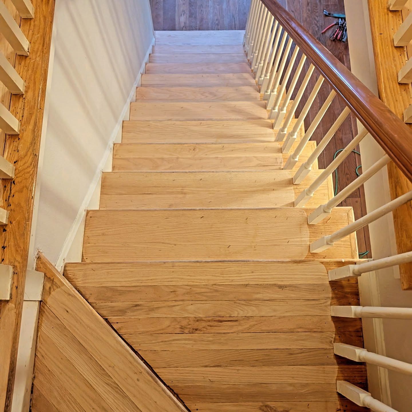Wooden staircase viewed from above with white railing and light walls on both sides