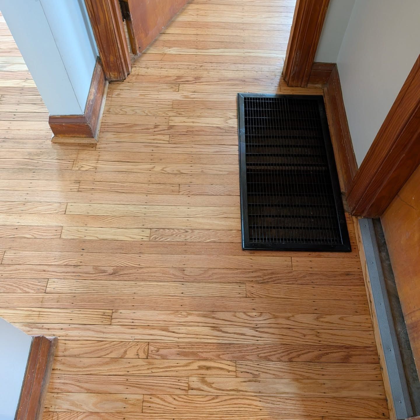 Hallway with wood flooring and a black floor vent near the wall