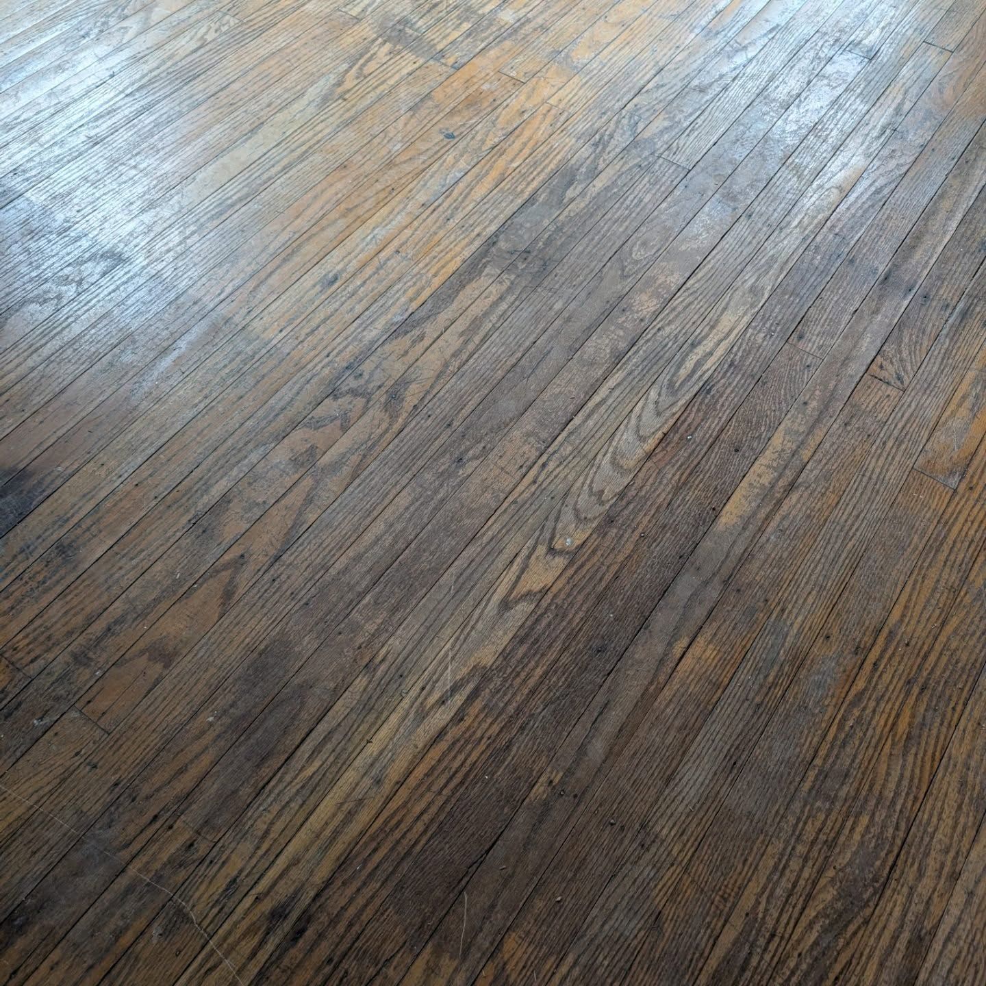 Weathered wooden floorboards with gray-brown grain and diagonal light reflections