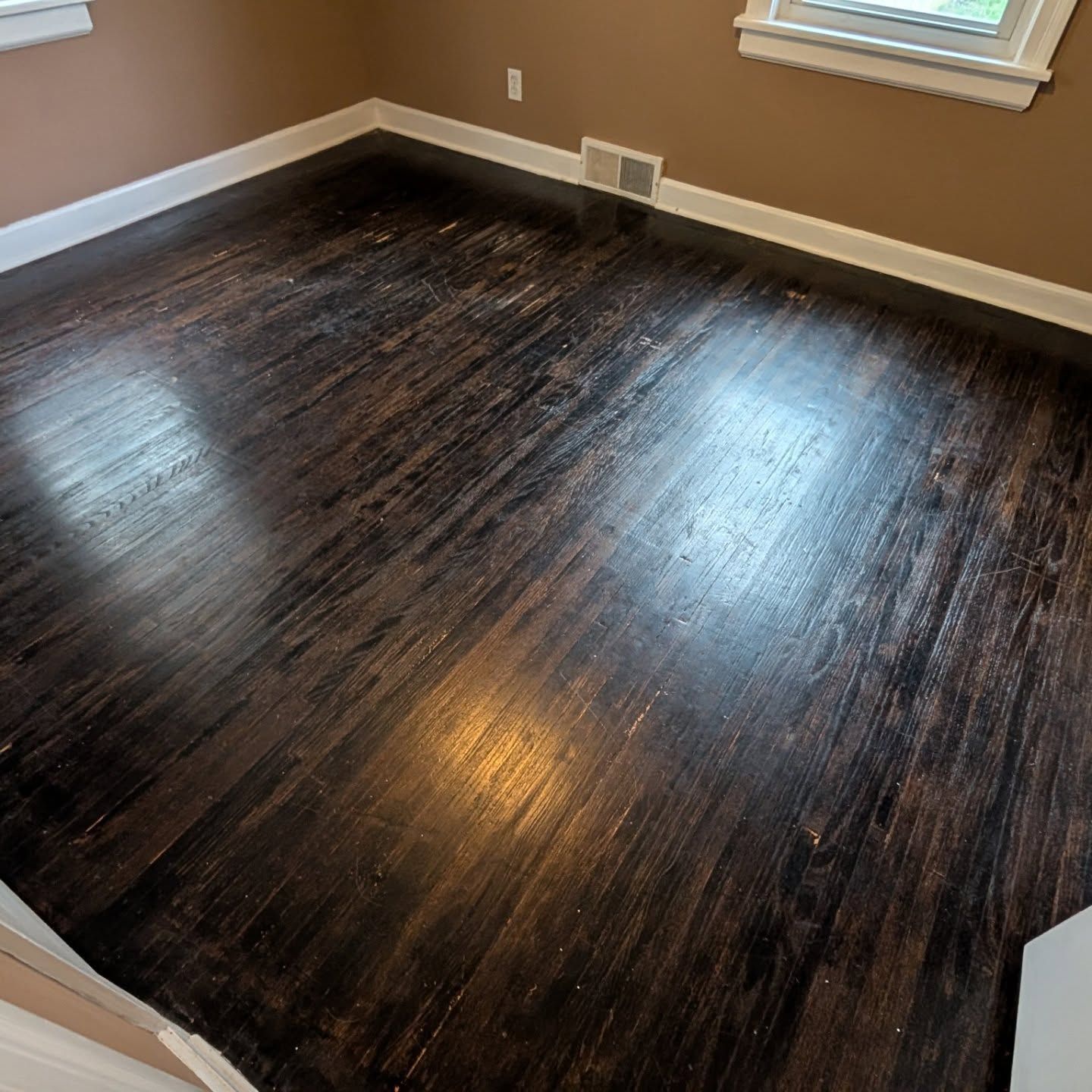 Empty room with dark hardwood floors, beige walls, white trim, and a window letting in light