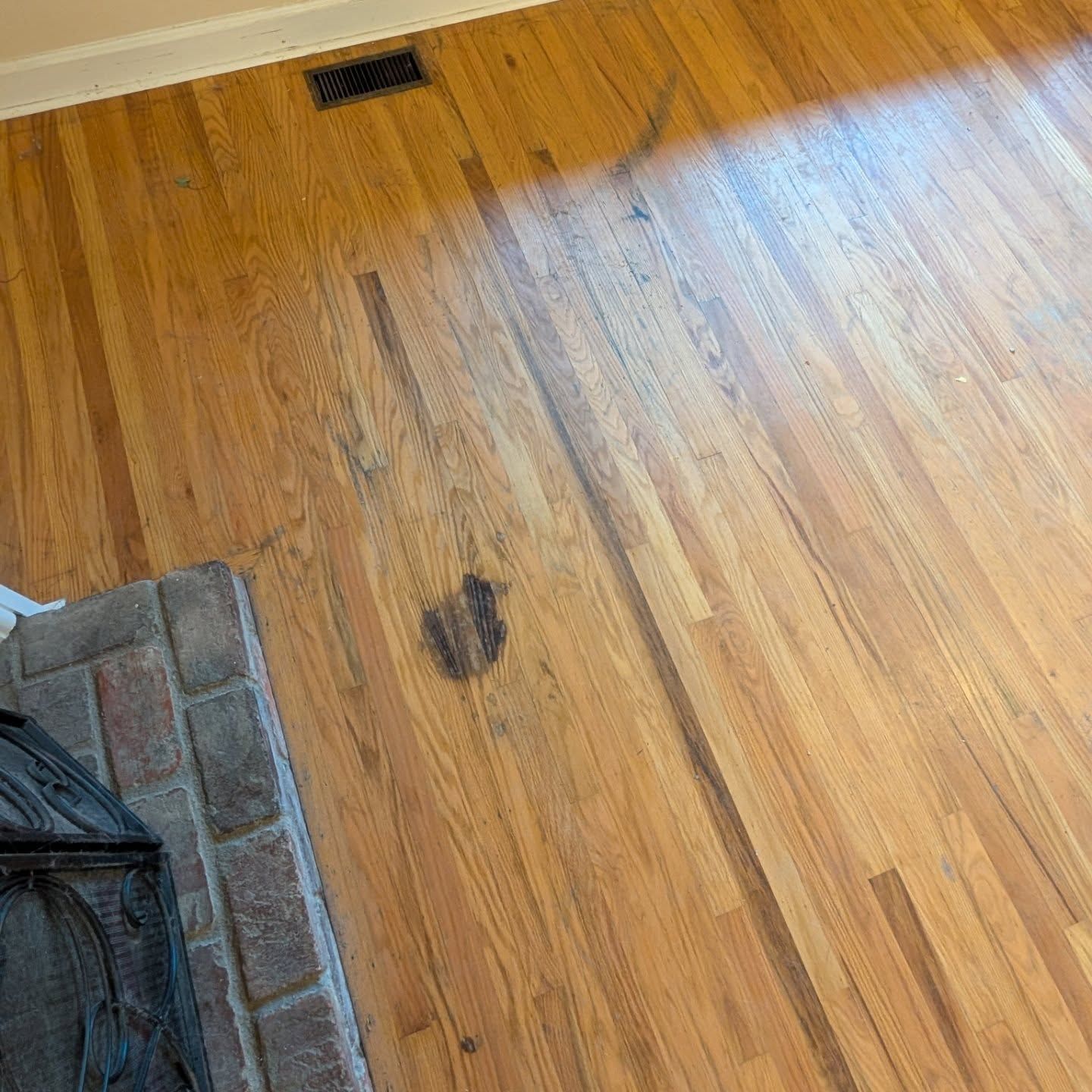 Wooden floor with a dark stain near a carpeted fireplace area