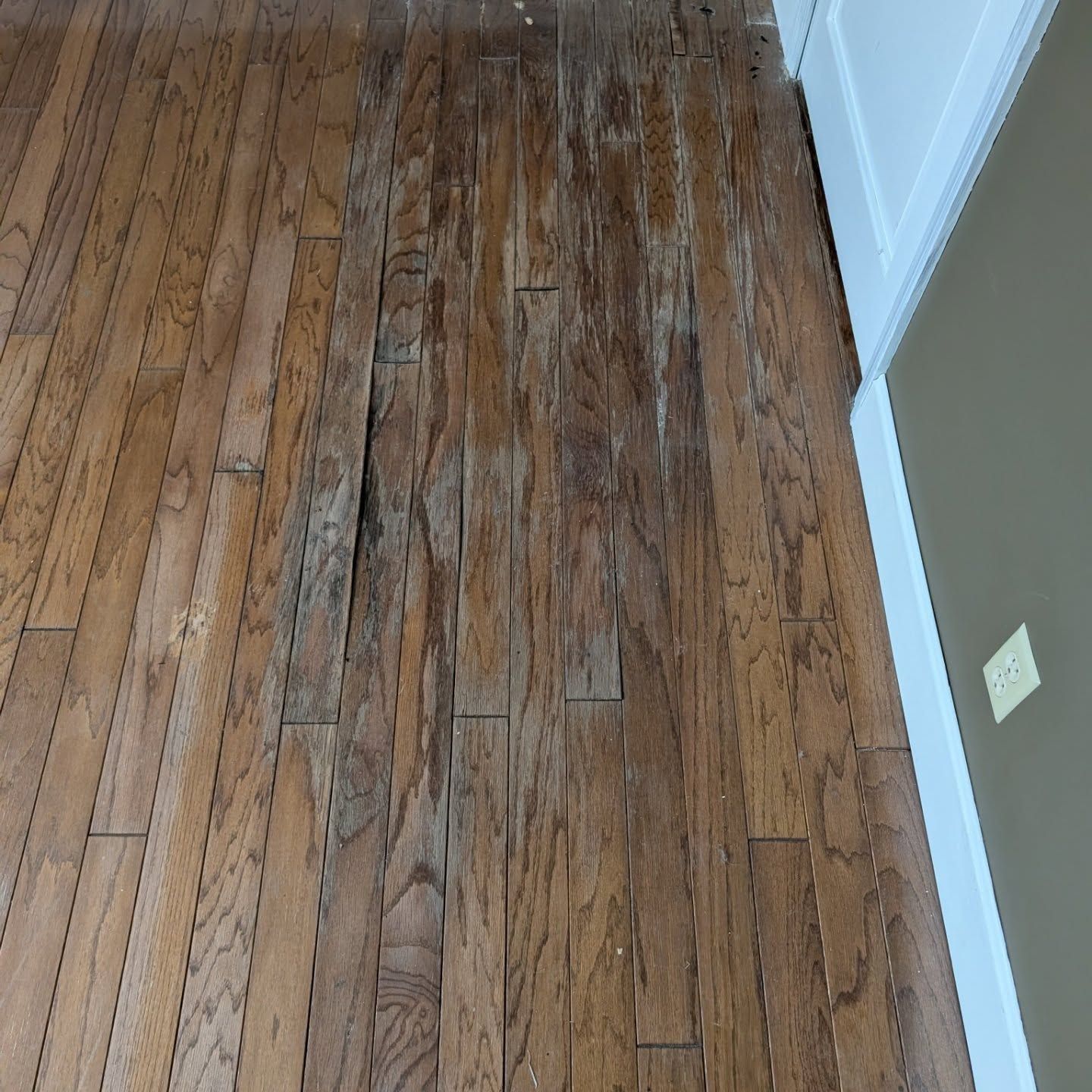 Wooden hardwood floor with worn, weathered planks beside a wall and electrical outlet.