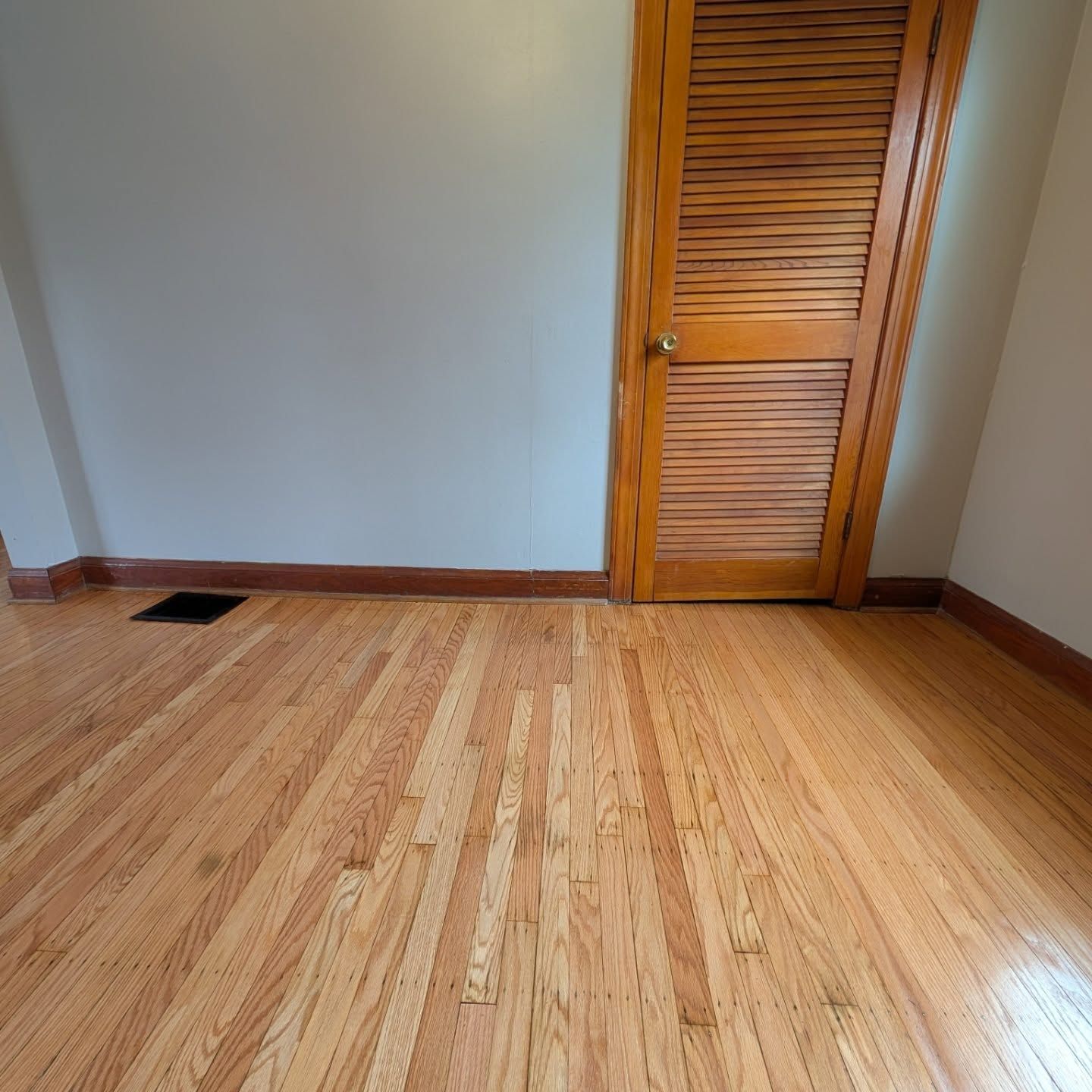 Empty room with light wood floor, beige walls, a wooden closet door, and a floor vent