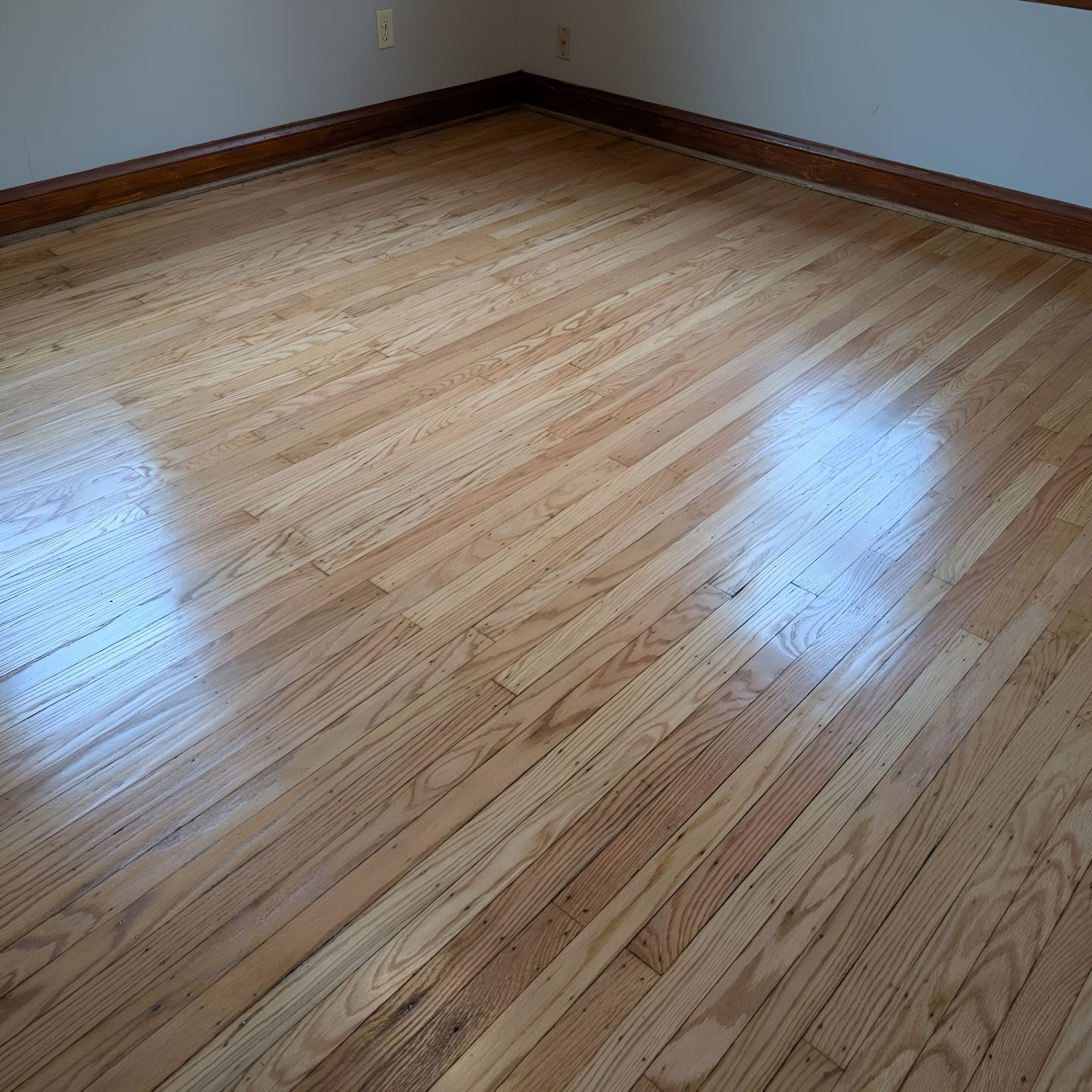 Empty room with glossy hardwood floors, white walls, and wood baseboards.