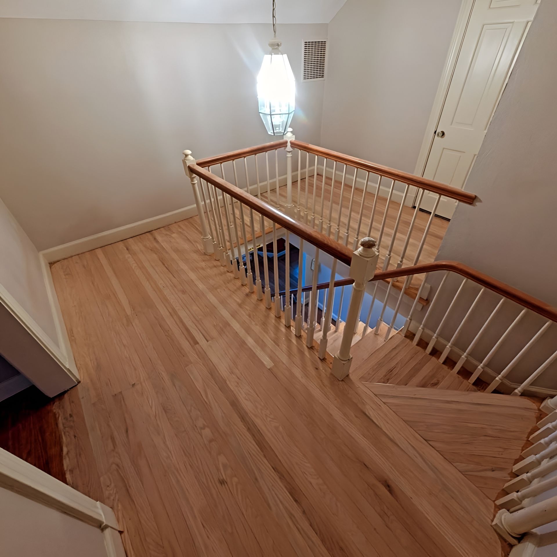Stairway landing with light wood floors, white banisters, and a hanging light fixture.