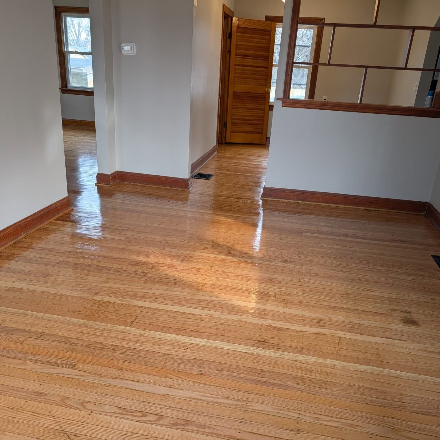 Empty room with polished hardwood floors, gray walls, and a doorway to a small hall.