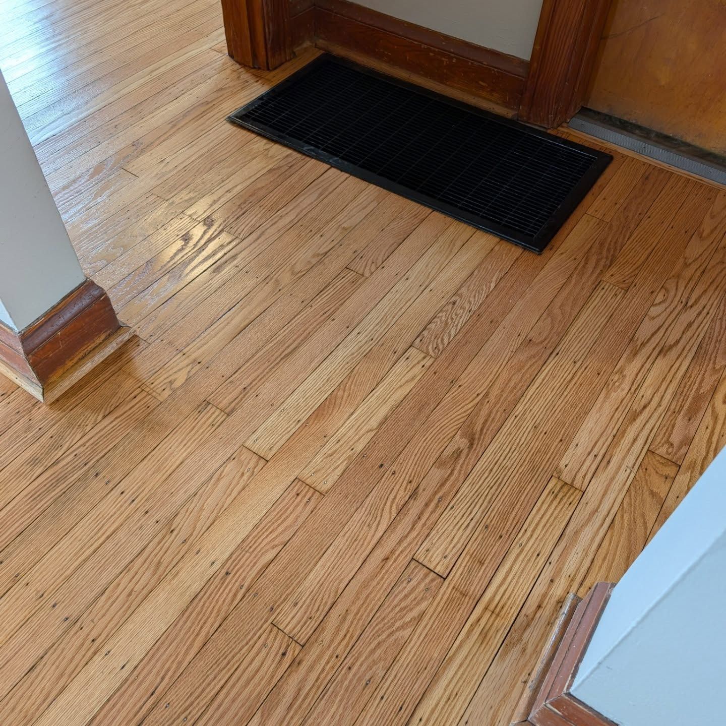 Wooden hallway floor with a black doormat near a doorway
