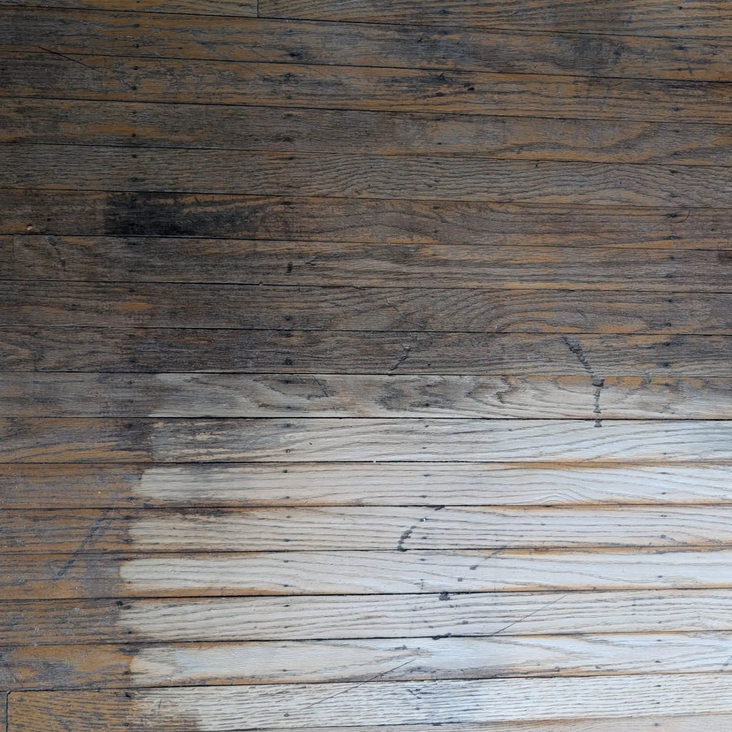 Weathered wooden surface with dark grain above and a lighter worn section below.