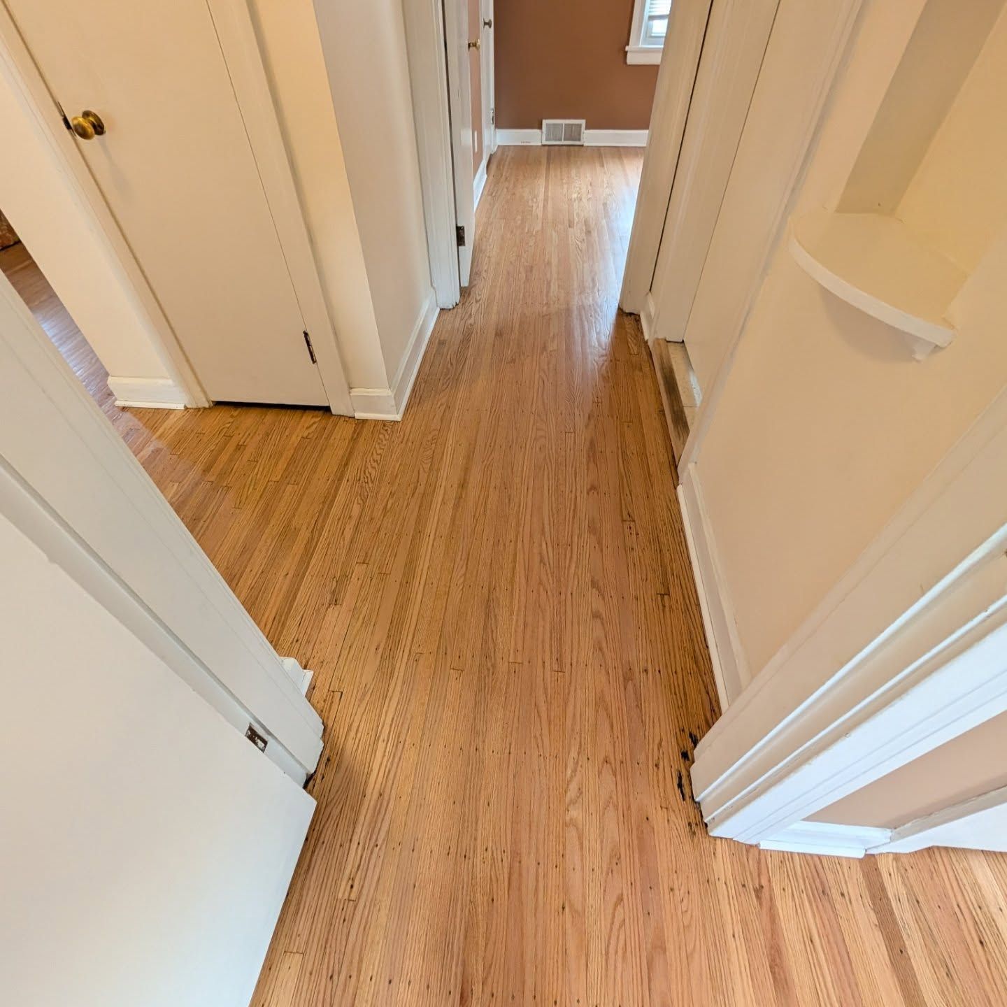 Narrow hallway with light wood flooring and white doors leading to a room at the end