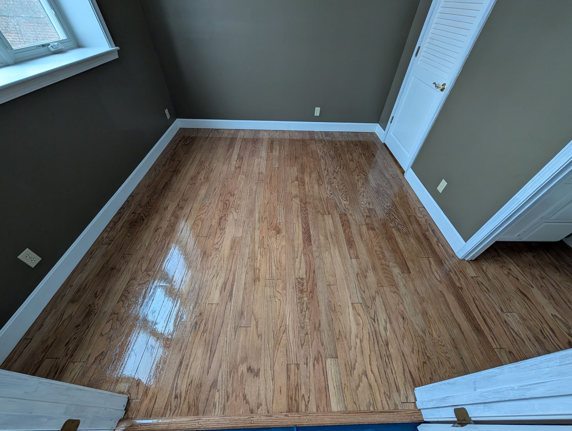 Empty small room with wood floor, gray walls, and a window on the left.