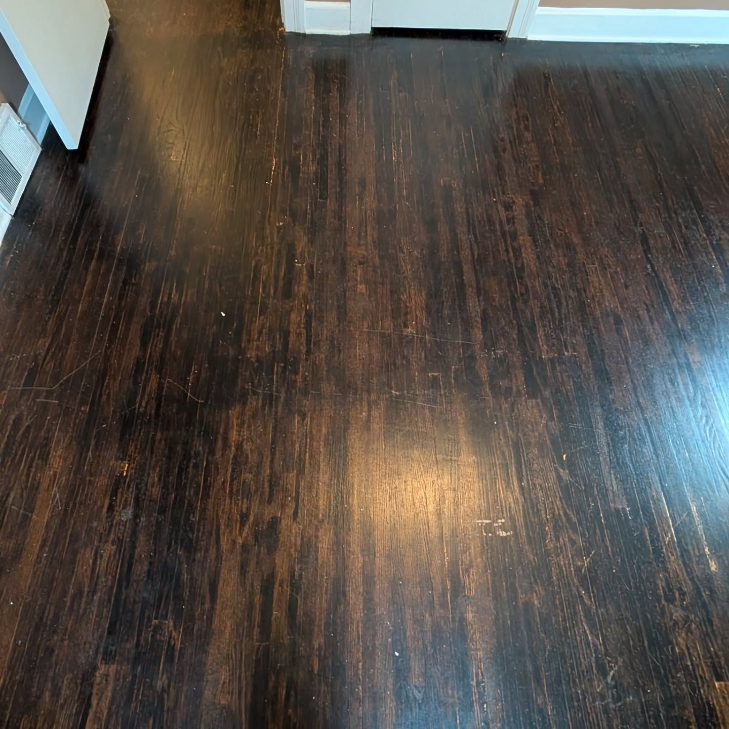 Dark hardwood floor in a hallway with white trim and light reflections.