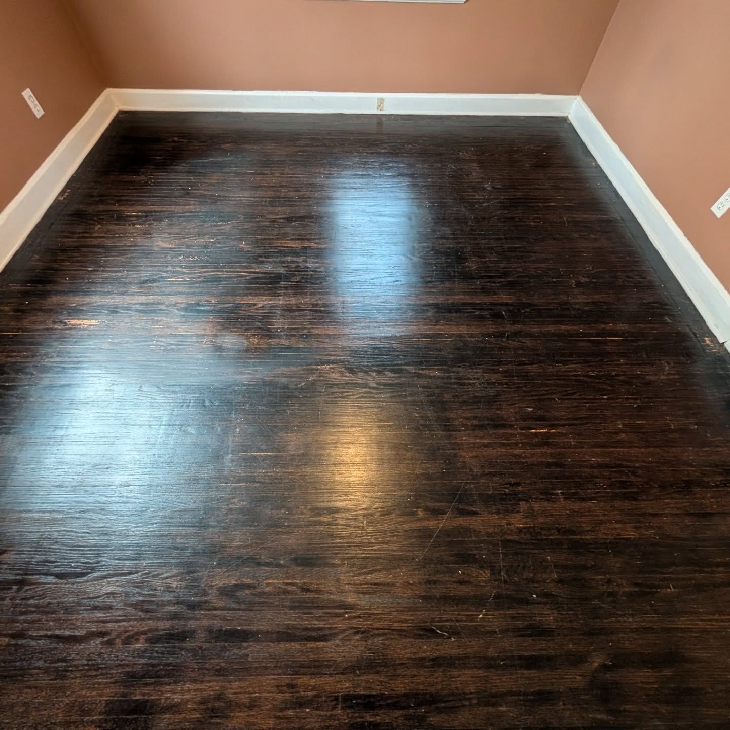 Empty room with dark wood floors, tan walls, and white baseboards.