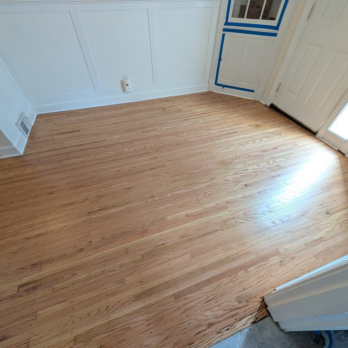 Empty room with light wood floor, white walls, and a sunlit doorway.