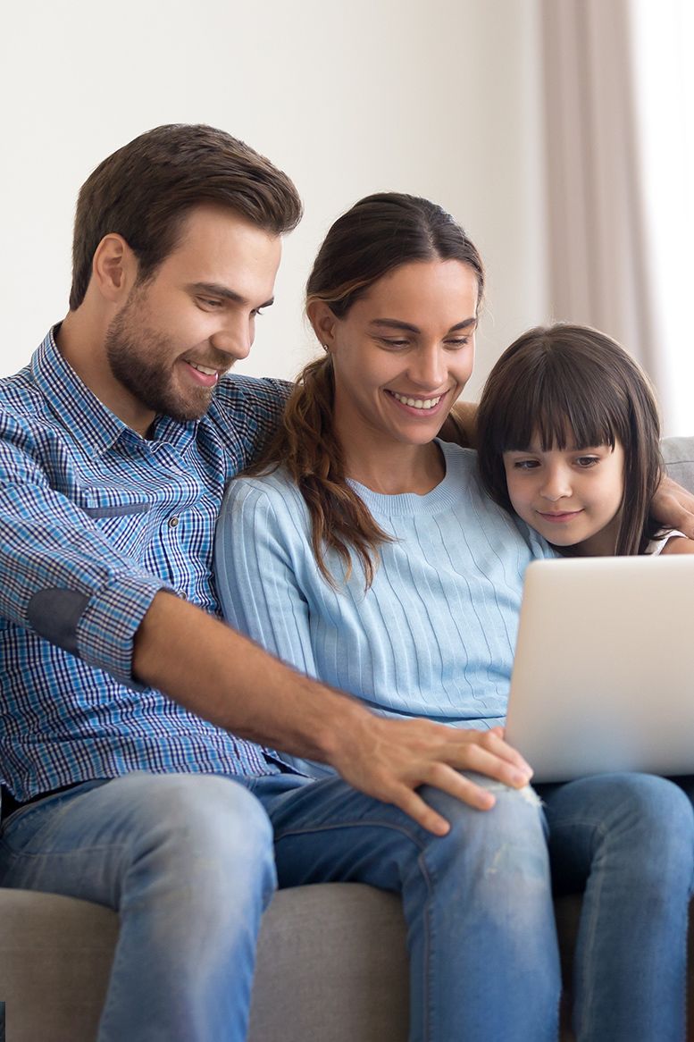 Family of three looking at a laptop on a couch, smiling.