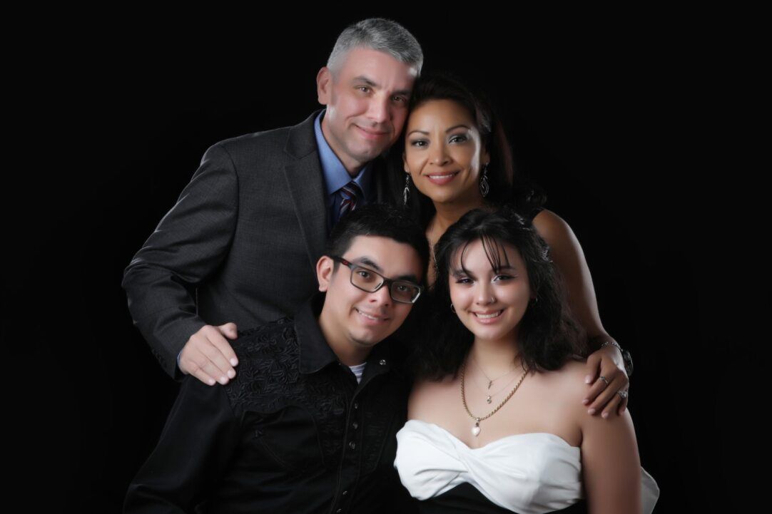 Family portrait: father with gray hair, mother, son, daughter in formal attire against black background.