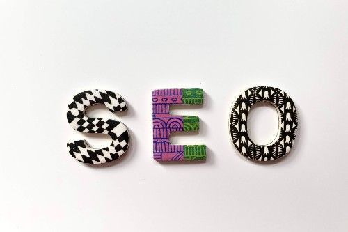 Lettres SEO en blocs 3D à motifs noirs et blancs, avec un E violet et vert sur fond blanc