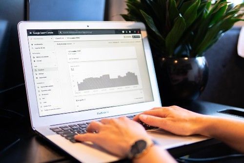 Des mains tapent sur un ordinateur portable affichant un tableau de bord analytique à côté d'une plante verte dans un espace de travail sombre
