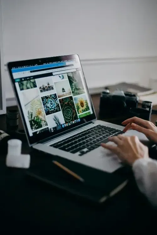 Une personne tape sur un ordinateur portable affichant un site web de design sur un bureau dans une pièce faiblement éclairée