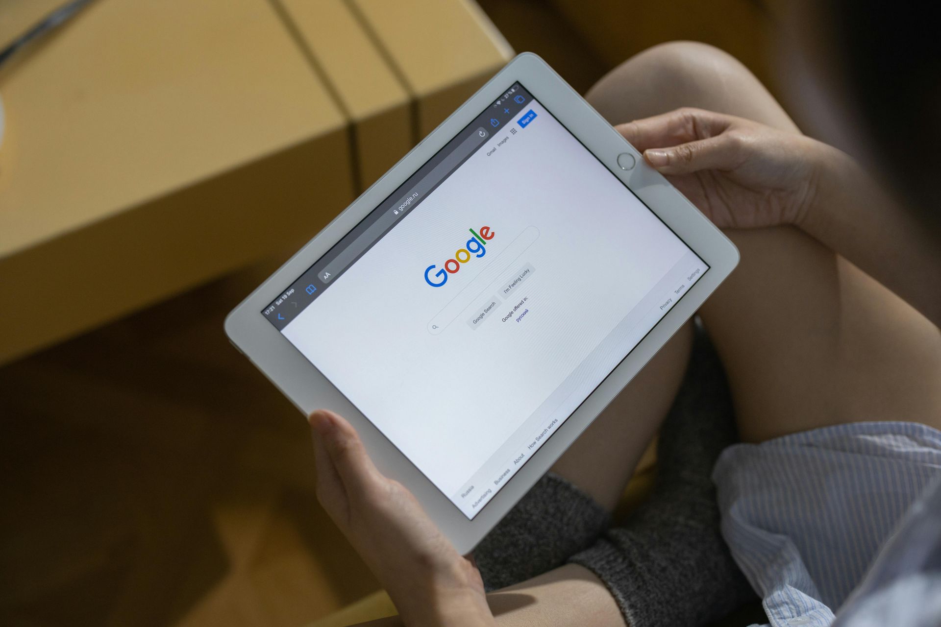 Une personne tenant une tablette blanche affichant la page d'accueil de Google à un bureau