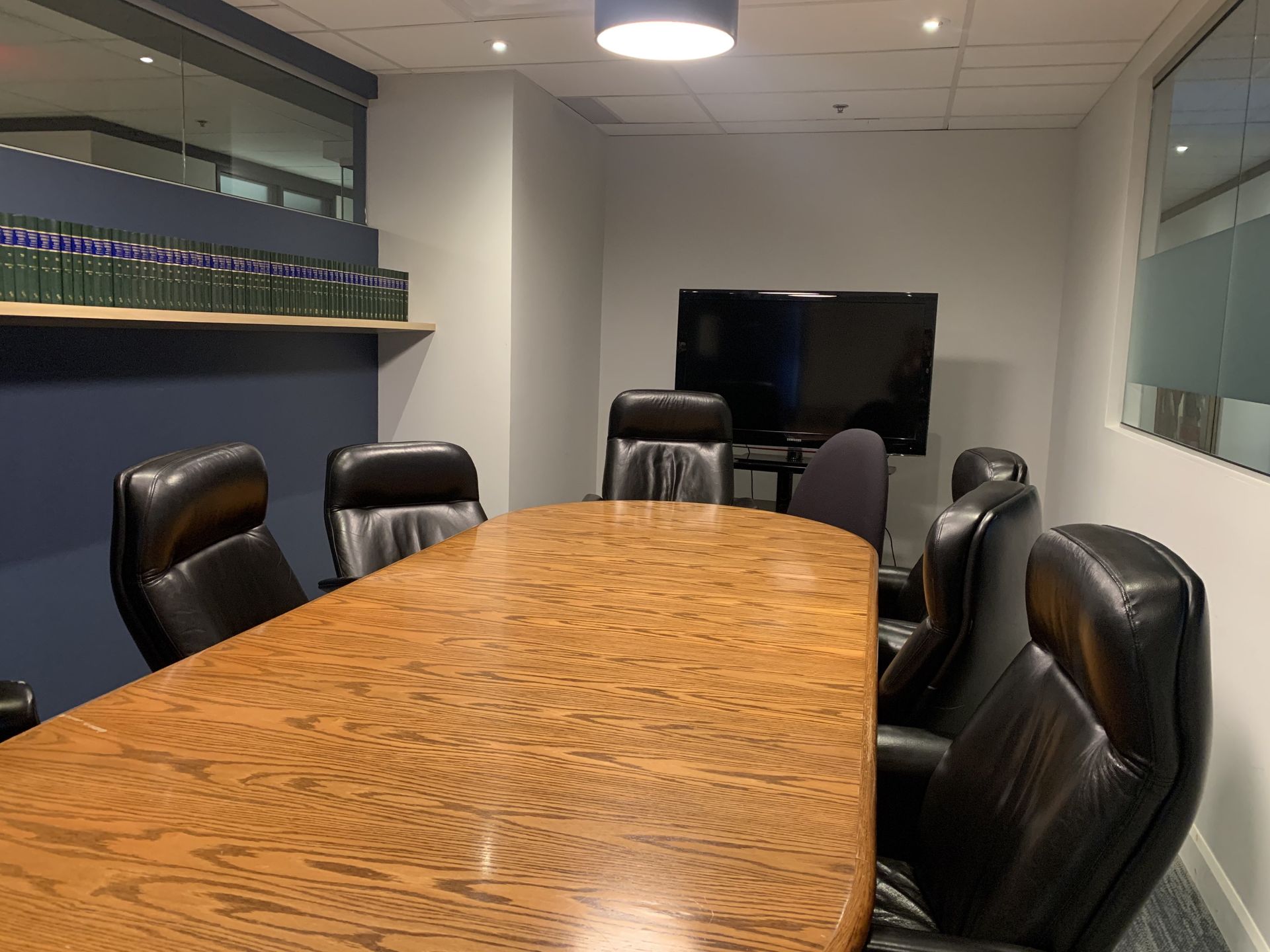 Conference room with a long wooden table, black leather chairs, and a wall-mounted TV.