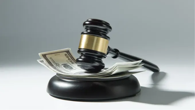 Marteau de juge posé sur une pile de billets de banque américains, sur un socle noir