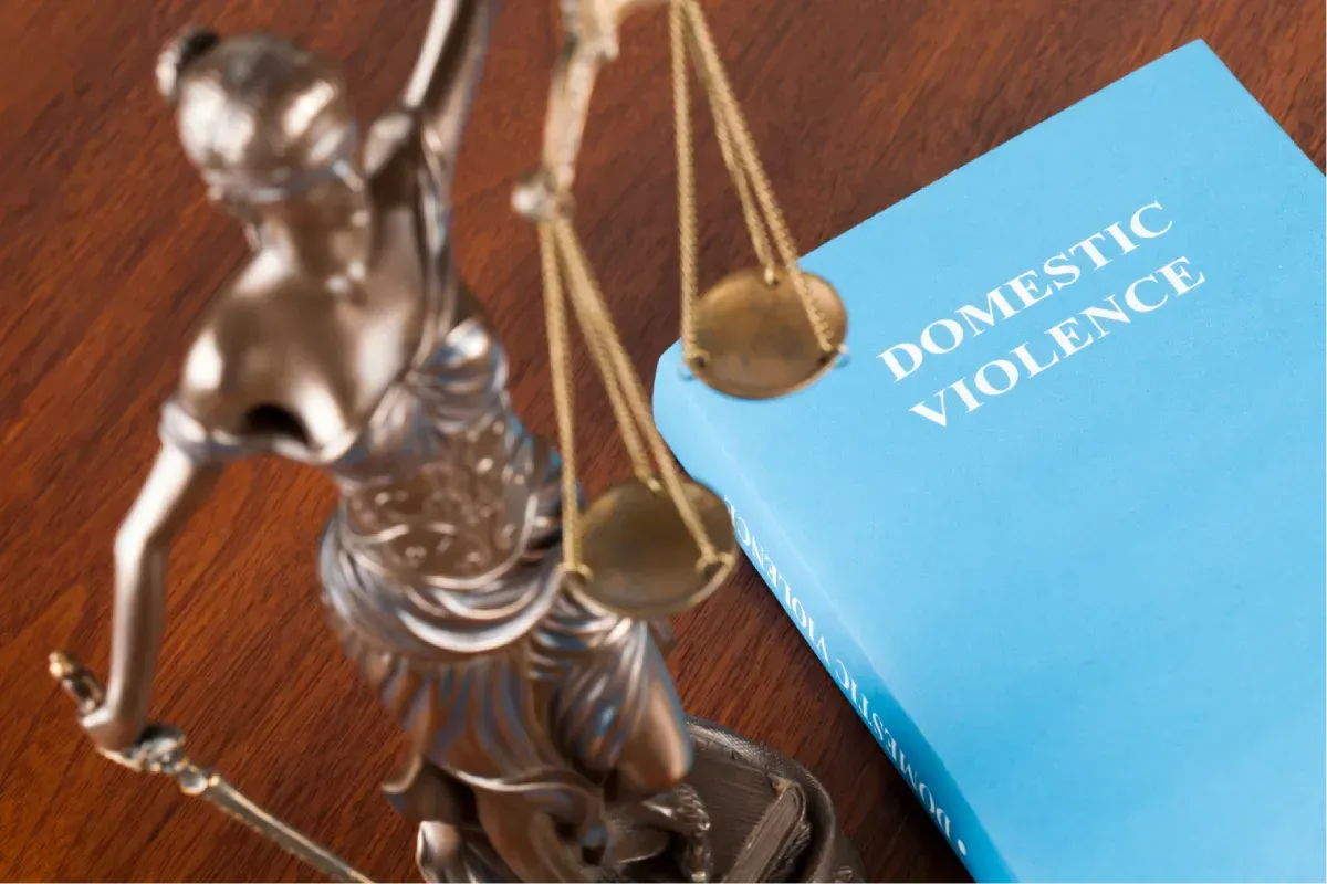 Justice scales beside a blue book labeled “Domestic Violence”