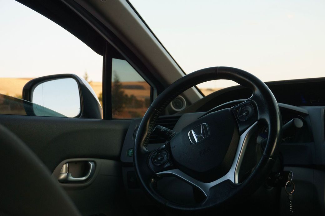 Intérieur de voiture avec volant, rétroviseur latéral et lumière du soleil couchant à travers la vitre