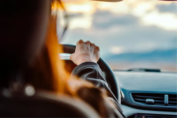 Les mains du conducteur sur le volant, vues de l’arrière, à l’intérieur d’une voiture au crépuscule