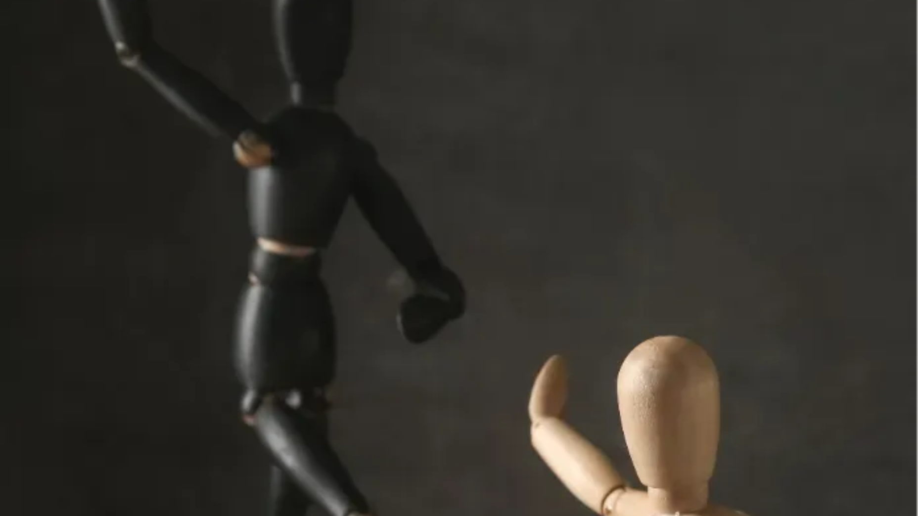 Deux mannequins en bois tendent la main l’un vers l’autre dans une scène faiblement éclairée.
