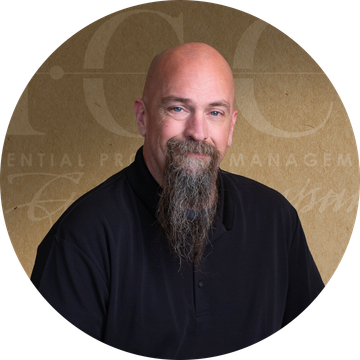 Bald man with a long beard, wearing a black shirt, posing for a headshot in front of a tan background.