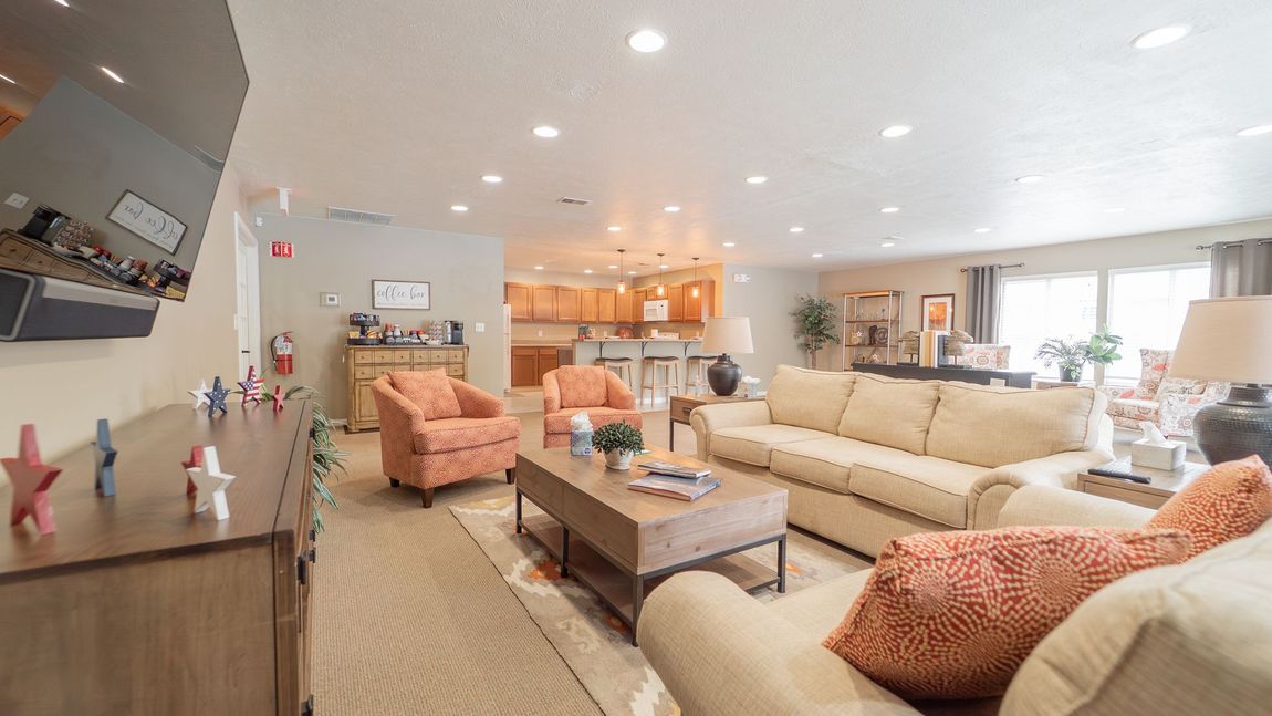 Spacious living room with tan sofa, orange armchairs, wooden coffee table, and open kitchen in the background.