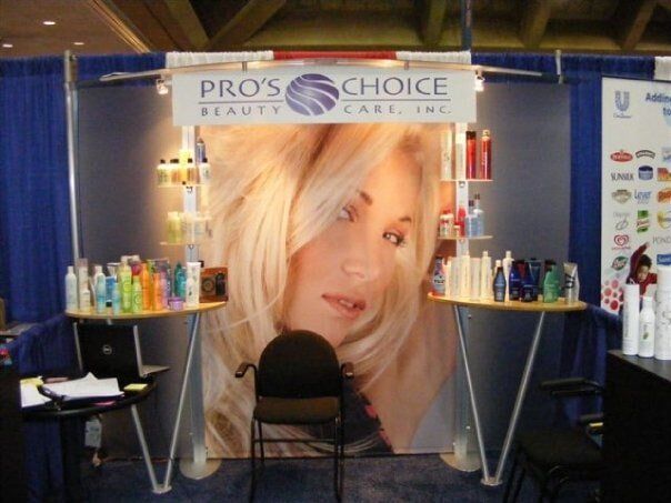 Pro's Choice Beauty Care booth at a convention; products displayed on tables, large woman's face in backdrop, logo overhead.