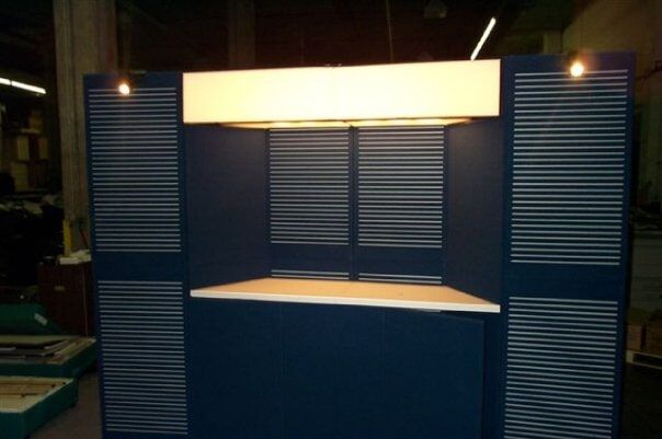Display booth with blue walls, horizontal slat details, a white countertop, and overhead lighting.